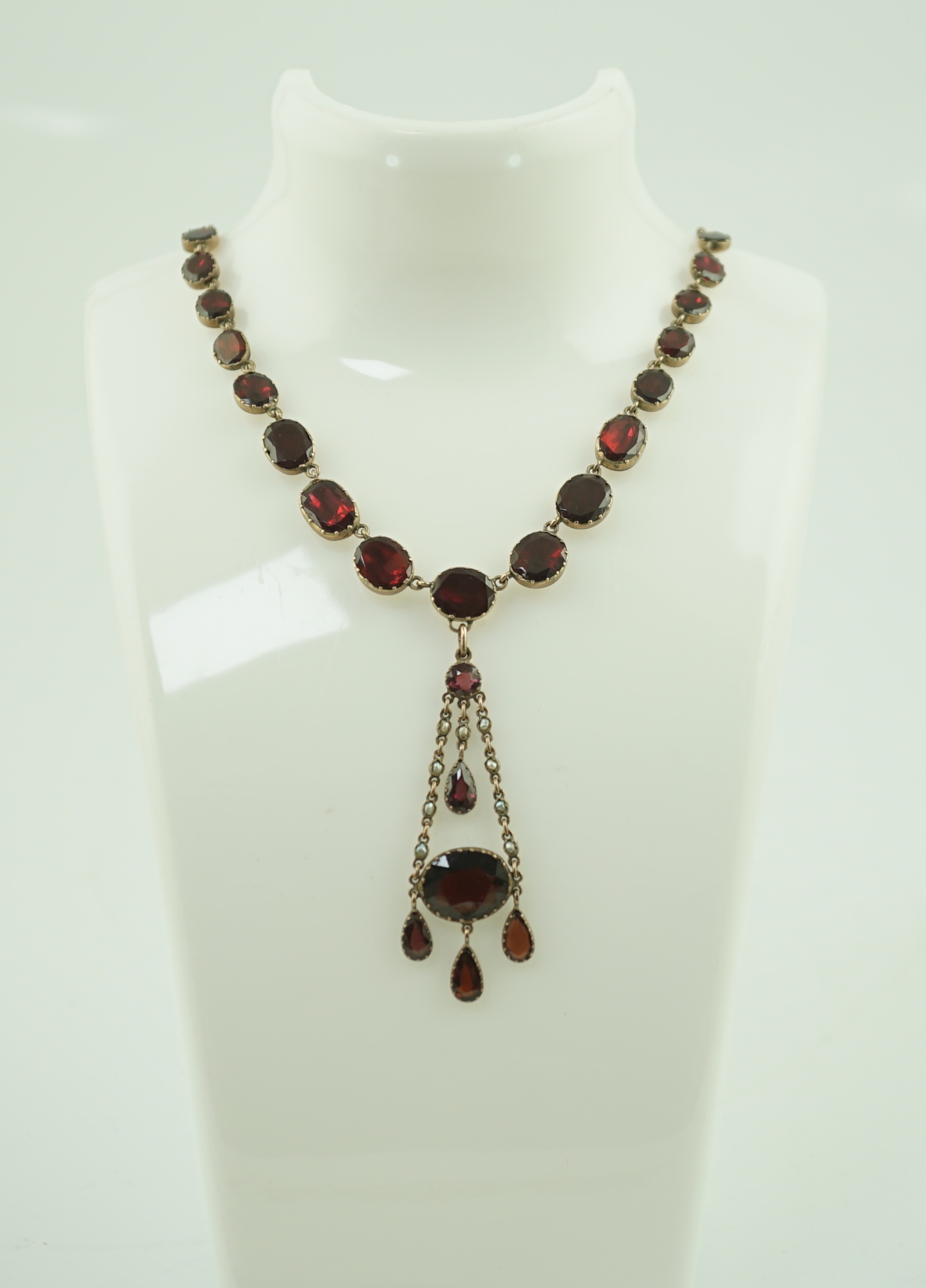 An early 19th century gold, and thirty five graduated foil backed garnet set necklace, with later garnet and seed pearl set drop
